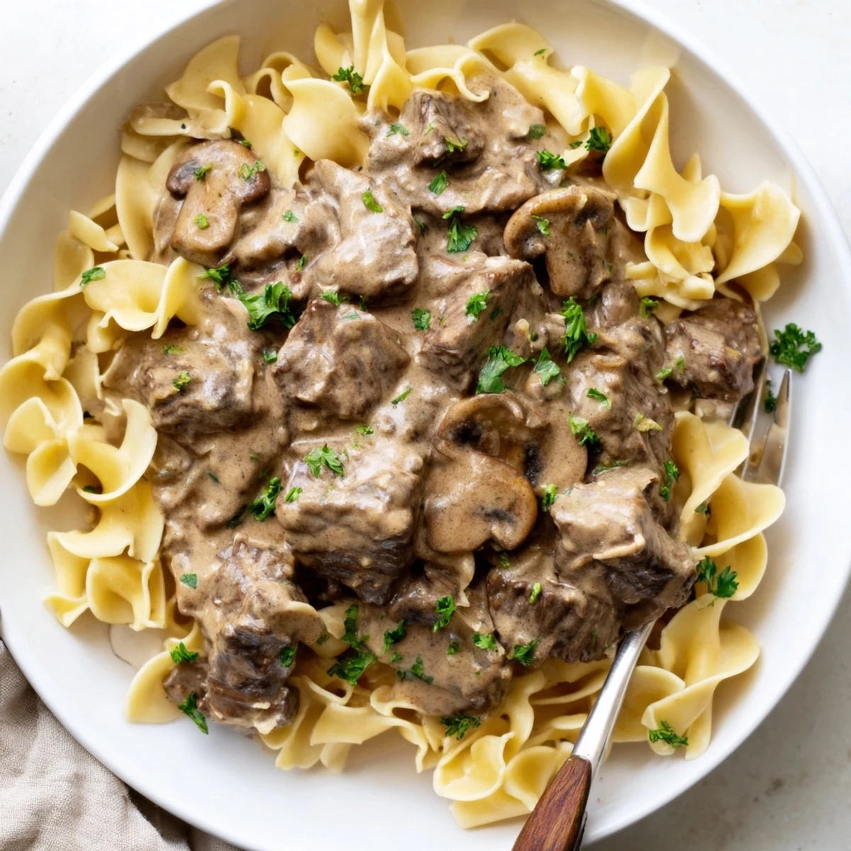 Tender slow cooker beef stroganoff poured over fluffy egg noodles, garnished with parsley.  