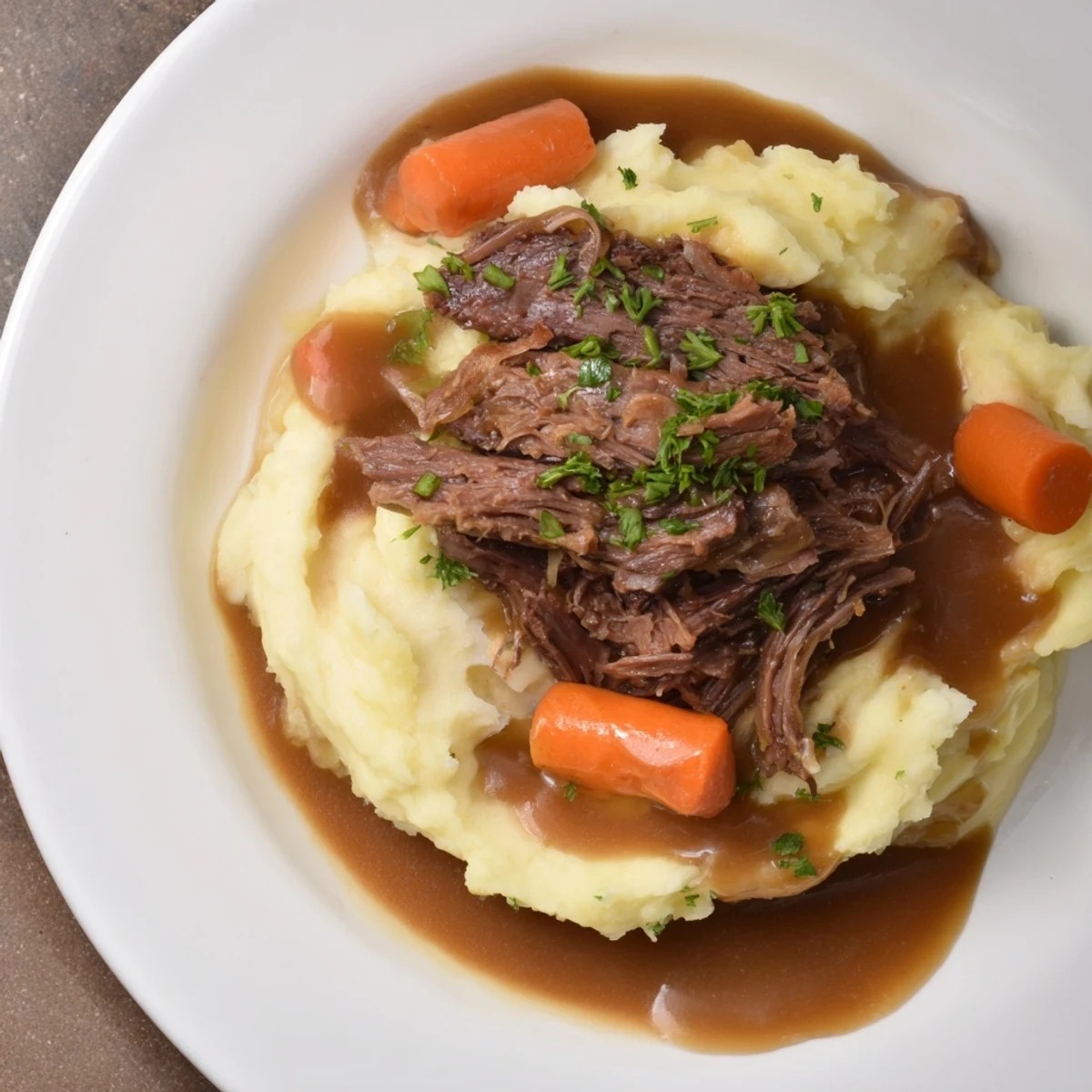 Tender Slow Cooker Pot Roast with vegetables and rich gravy served atop creamy mashed potatoes.