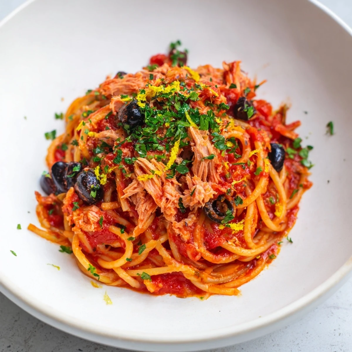 Pasta with tuna, olives, and capers, a savory dish with flaky tuna and bright green parsley.