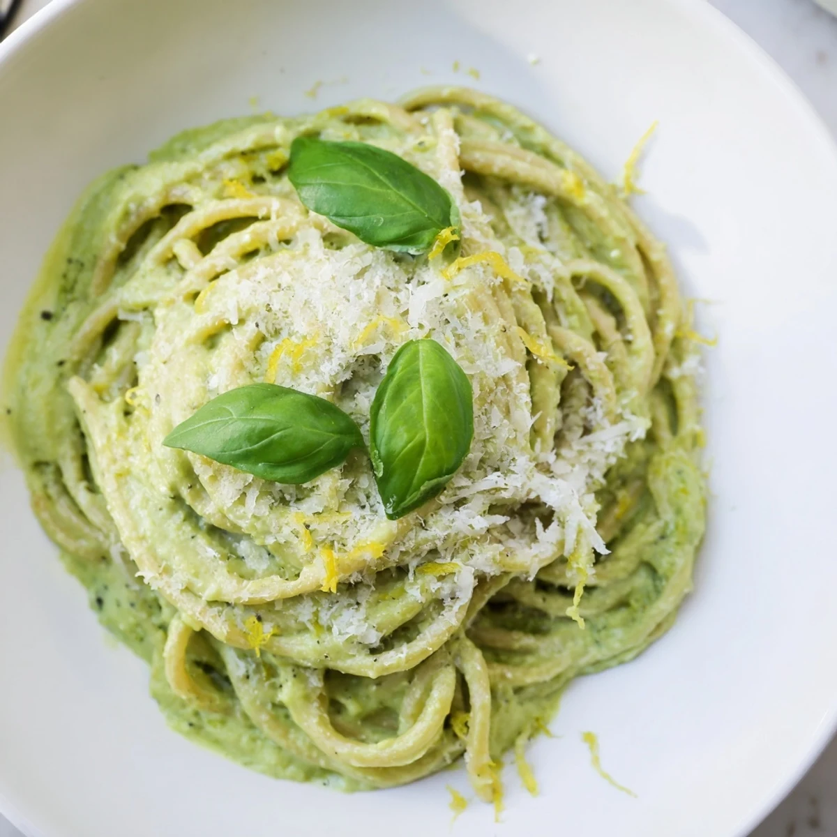 Creamy avocado pasta, a bright green dish, topped with fresh basil and Parmesan cheese ready to enjoy.