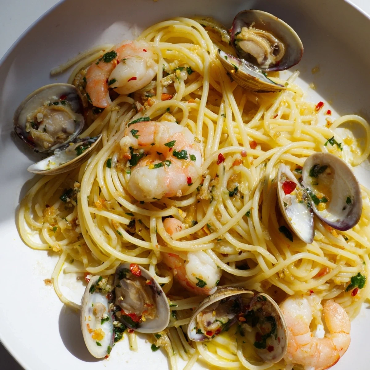 Steaming plate of Seafood Pasta Aglio e Olio with plump shrimp, clams, and perfectly cooked spaghetti.