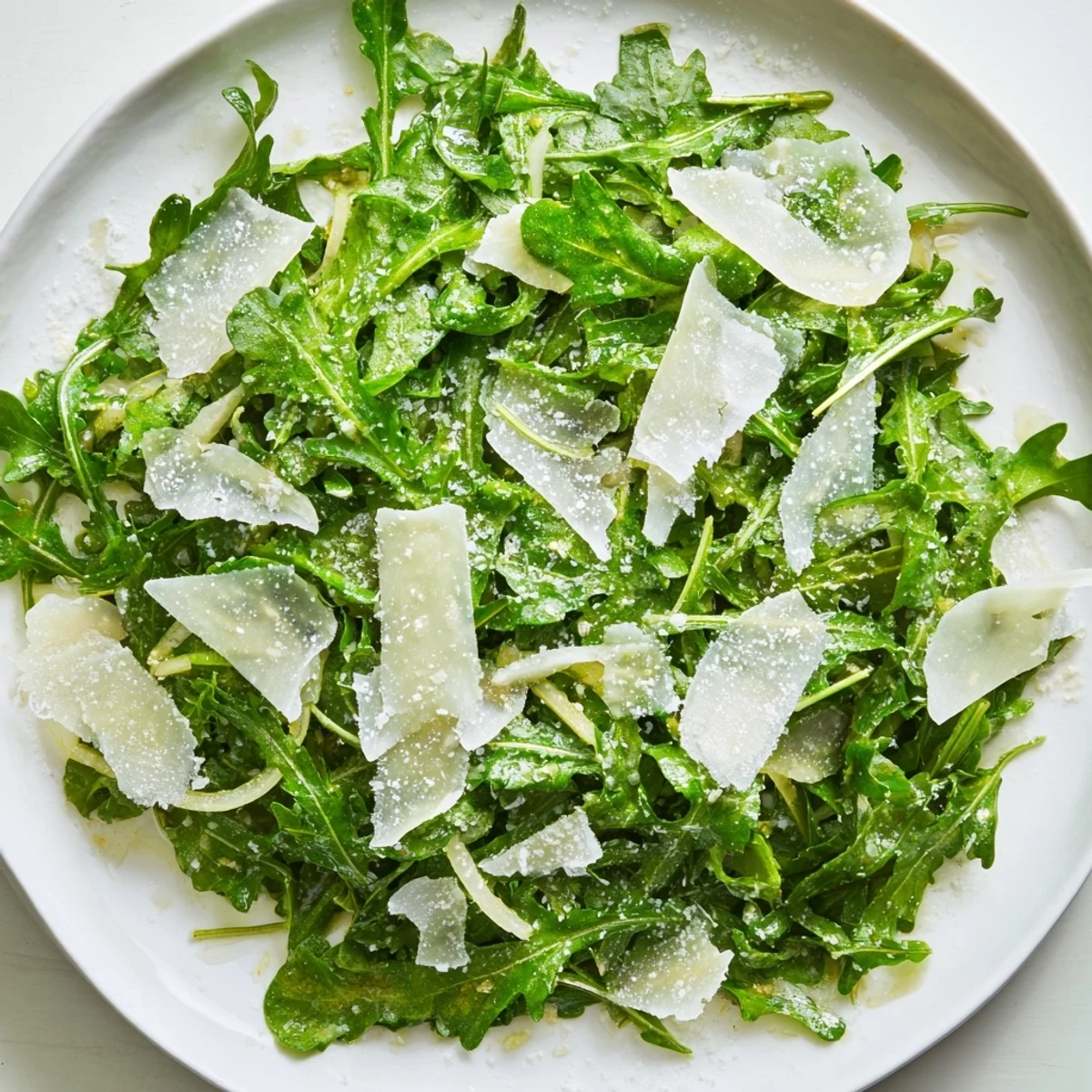 Fresh arugula salad with bright lemon dressing, Parmesan shavings on top; tastes zesty and refreshing.