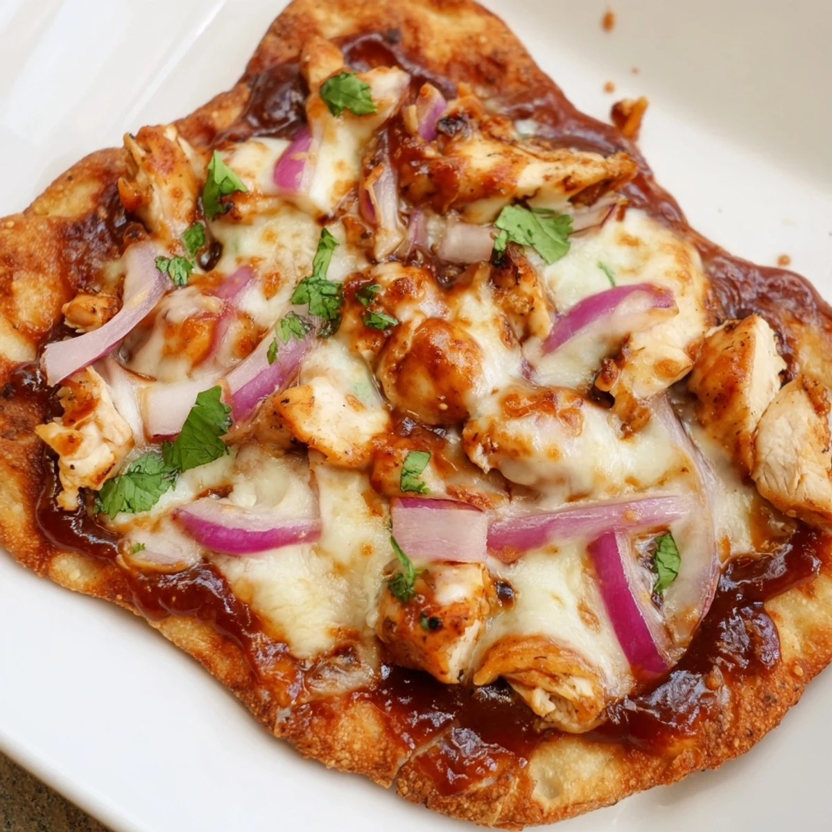 Freshly baked BBQ Chicken Flatbread topped with tender grilled chicken, sweet red onions, and gooey mozzarella cheese, served on a wooden cutting board.