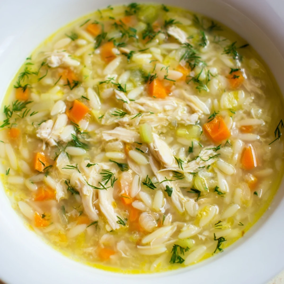 Steaming pot of Chicken Lemon Orzo Soup, filled with carrots, celery, and shredded chicken in a golden broth.