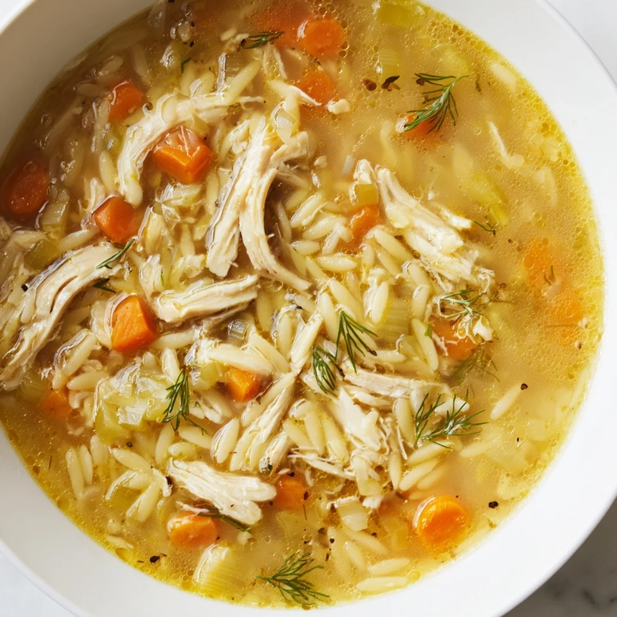 Comforting Chicken Lemon Orzo Soup in a rustic bowl, lemon zest and fresh herbs visible for a bright Mediterranean meal.