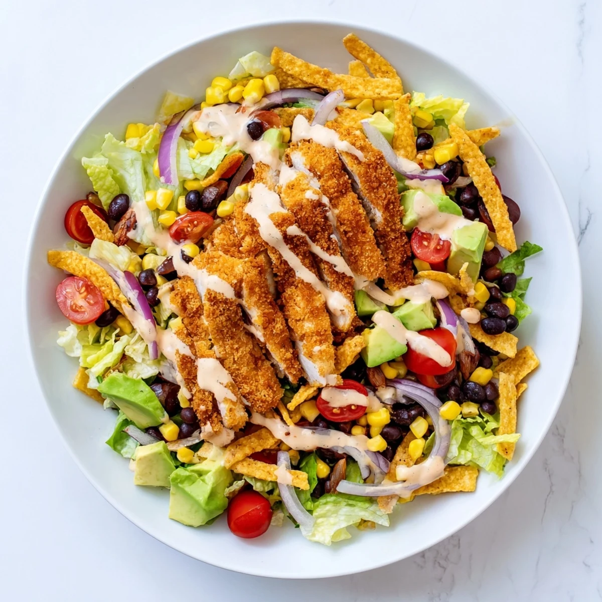 Golden crispy chicken strips rest on a bed of romaine lettuce, tomatoes, corn, black beans, and avocado, drizzled with creamy salsa ranch in a vibrant Tex-Mex salad.  