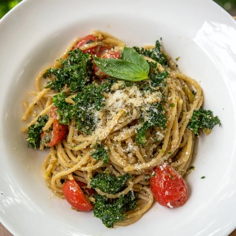 Steaming one-pot spaghetti with kale and tomatoes, topped with fresh basil, ready to serve.