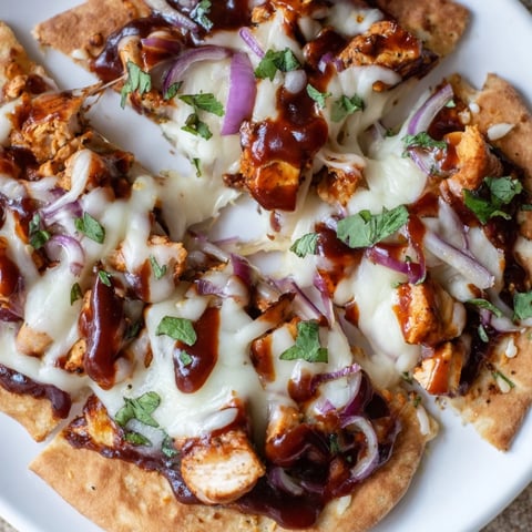 A close-up of BBQ Chicken Flatbread with melted mozzarella, grilled chicken, and sliced red onion on a crispy crust, drizzled with tangy BBQ sauce.