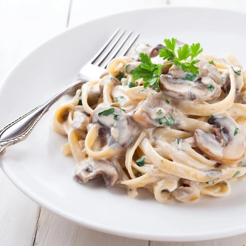 A steaming plate of Creamy Mushroom Alfredo pasta, featuring golden sautéed mushrooms and fresh parsley garnish.  