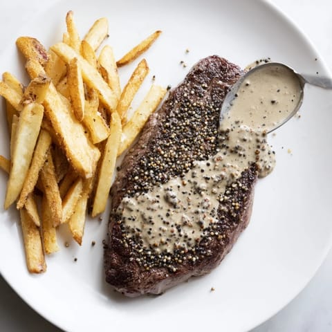 Perfectly seared Classic Peppercorn Ribeye with a peppercorn crust next to a pile of golden-brown fries.