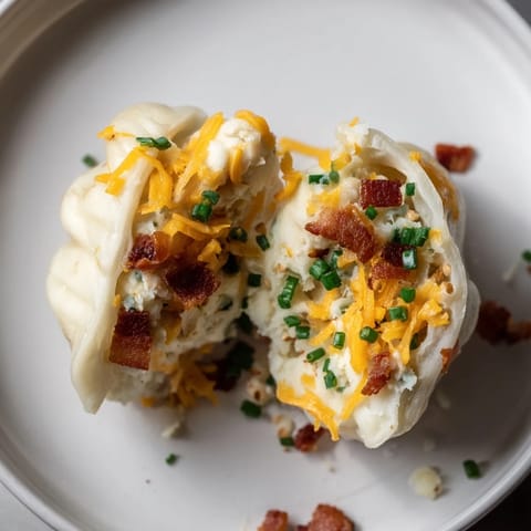 Close-up of freshly cooked loaded baked potato soup dumplings, piled high and garnished with chives and sour cream.