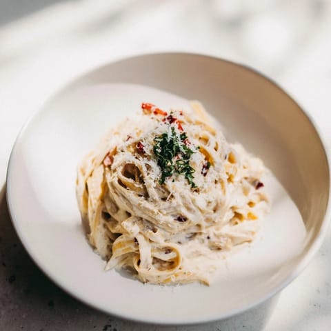 Creamy Skinny Alfredo Garlic Parmesan Snowy Pasta, glistening from the parmesan, promises a comforting, guilt-free meal.