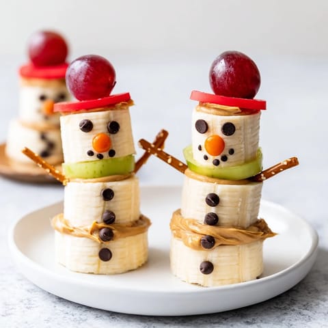 These tasty Banana Peanut Butter Snowmen stand tall, showcasing cheerful faces and pretzel arms, ready to enjoy!