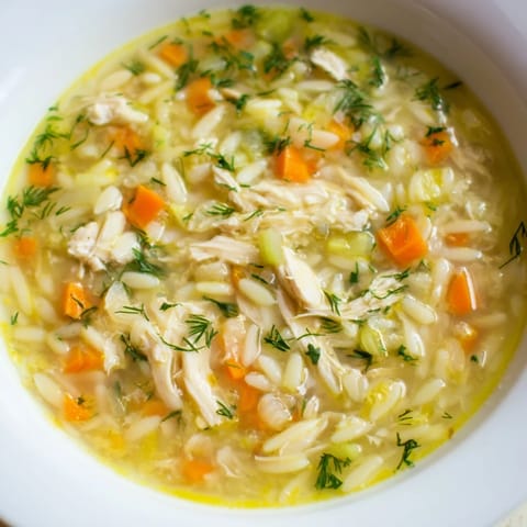 Steaming pot of Chicken Lemon Orzo Soup, filled with carrots, celery, and shredded chicken in a golden broth.