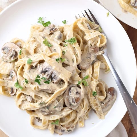 Close-up of Creamy Mushroom Alfredo in a white bowl, showing rich parmesan sauce coating fettuccine.  