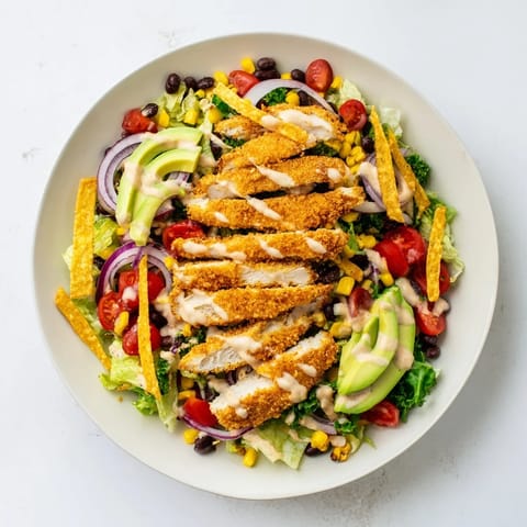 A close-up of the Crispy Chicken Taco Salad highlights crunchy tortilla strips, melted cheddar, and juicy avocado chunks alongside spiced chicken pieces.  