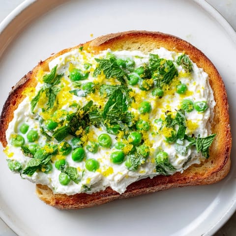Savory Pea & Mint Ricotta Toast served on a rustic wooden board, garnished with olive oil drizzle and lemon wedges for serving.