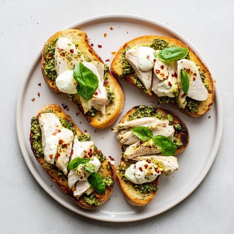 A close-up of pesto chicken burrata toast, where melted burrata drapes over juicy chicken and herbaceous pesto on toasted sourdough.