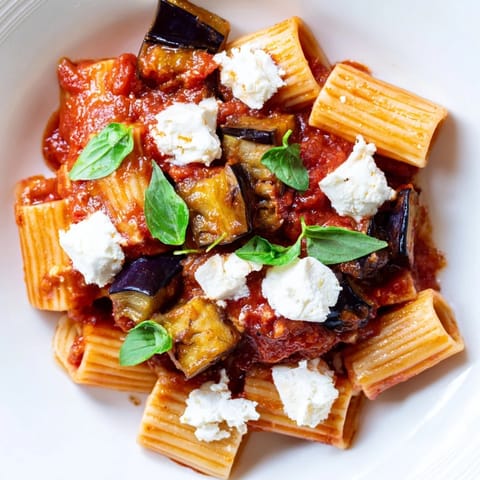 Pasta Alla Norma served in a white bowl, topped with grated ricotta salata and vibrant basil leaves.  