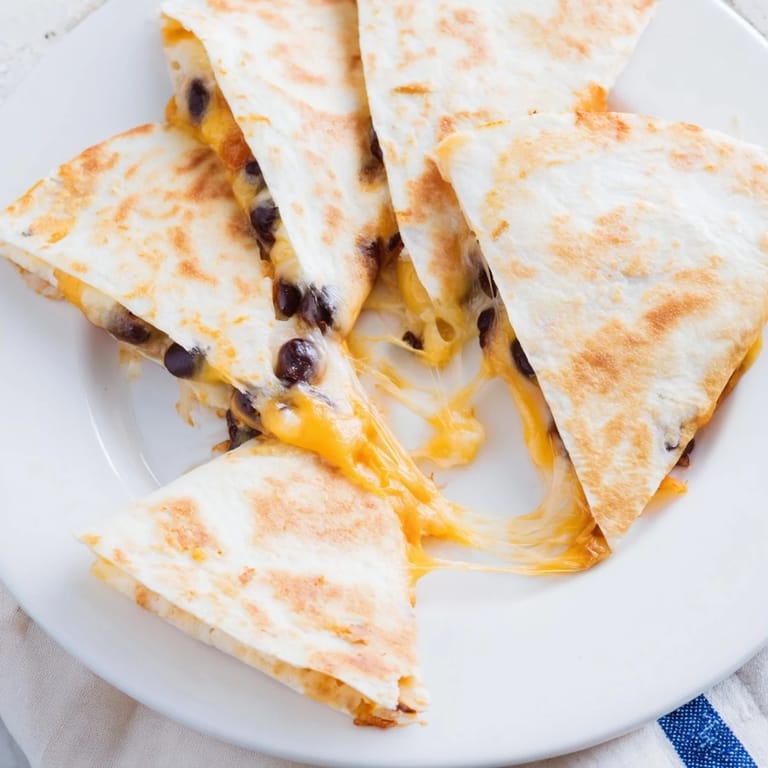 Melted cheese spills from a folded Bean & Cheese Quesadilla, ready to serve with fresh salsa and toppings.