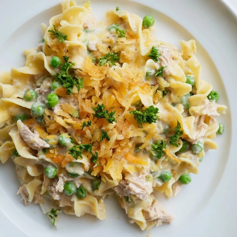Golden, baked tuna noodle casserole glistens with creamy sauce, fresh herbs, and a crunchy topping.