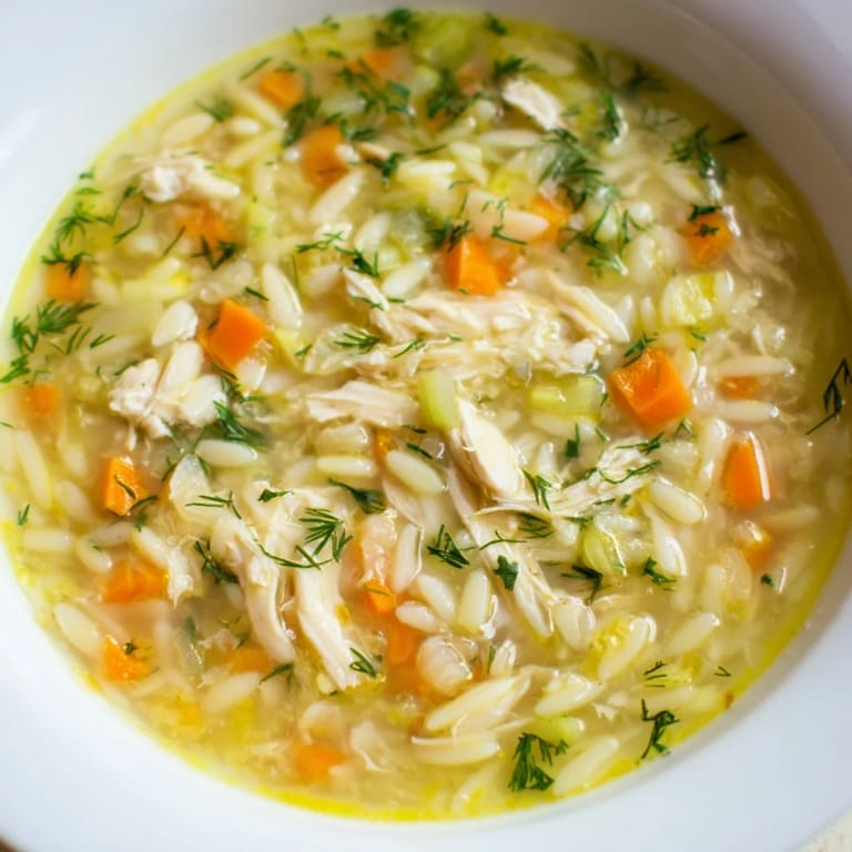 Steaming pot of Chicken Lemon Orzo Soup, filled with carrots, celery, and shredded chicken in a golden broth.