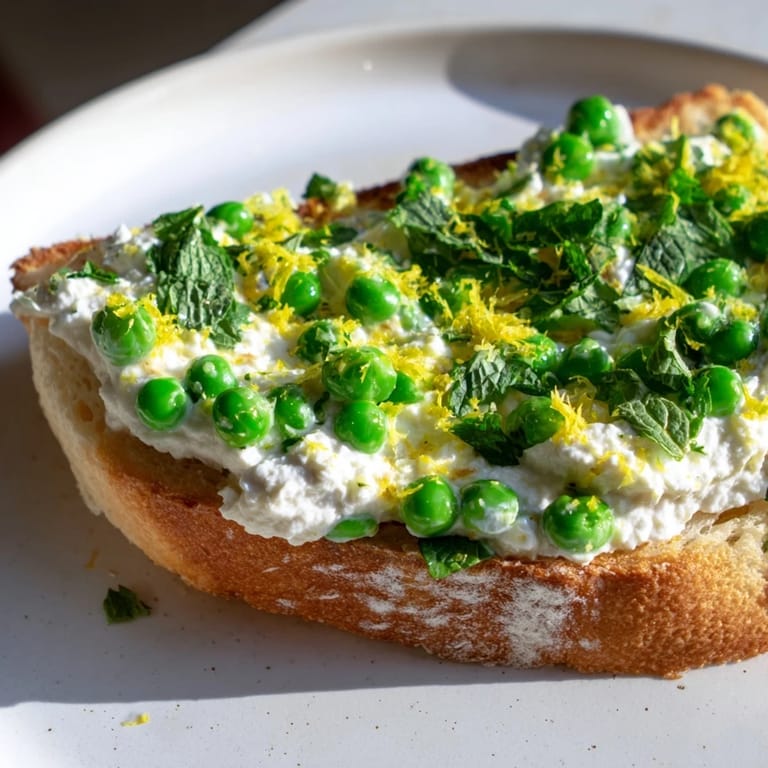 Easy vegetarian breakfast toast with smooth ricotta and sweet peas, finished with aromatic mint and zesty lemon on toasted sourdough.