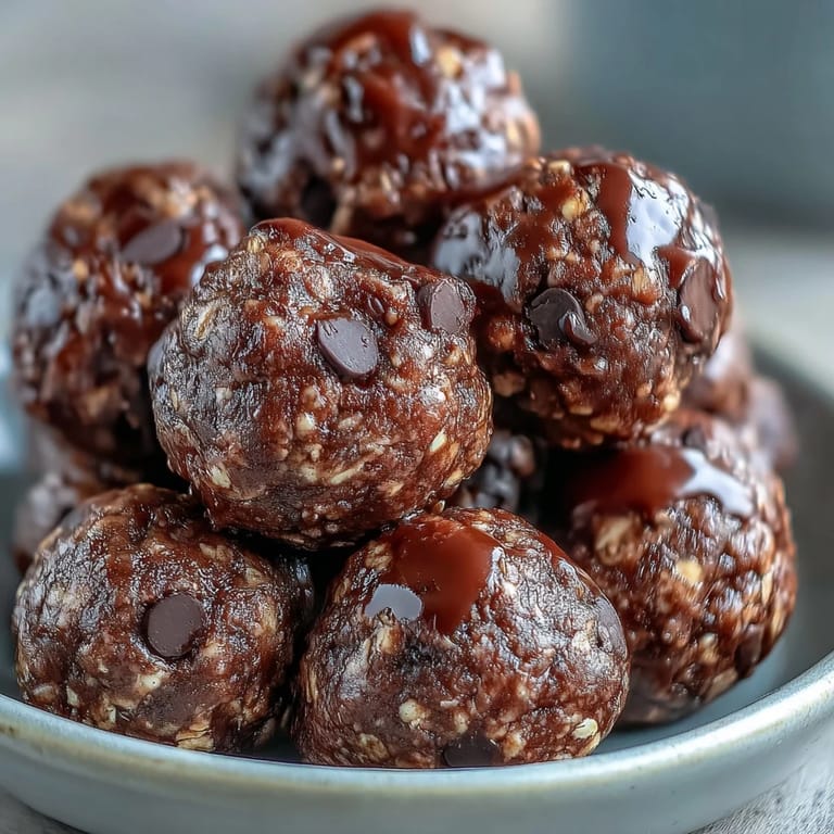 A close-up view of hand-rolled vegan chocolate peanut butter protein balls on a dark surface, dusted with extra cocoa powder, highlighting the fudge-like texture and energy-boosting ingredients.