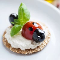 Creamy Ladybug Love Picnic Finger Foods topped with halved tomatoes and black olive heads.